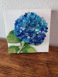 a blue flower made out of glass on top of a wooden table next to a white wall