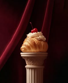 a cupcake sitting on top of a white pedestal next to a red drapes