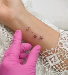 a person wearing pink gloves holding up a small tattoo on their left arm and paw prints on the wrist