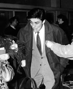 an old black and white photo of two people in suits walking through a room with other people