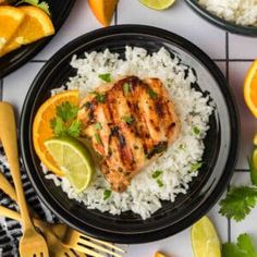 grilled chicken with rice, oranges and limes on a plate next to utensils