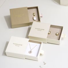 three jewelry boxes with necklaces in them on a white table next to other items