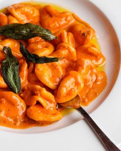 a white plate topped with pasta covered in sauce and sage leaves next to a spoon