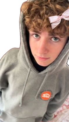 a young boy with curly hair wearing a gray hoodie and a pink bow on his head