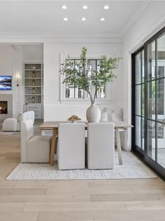 a living room with white furniture and a fireplace in the corner, surrounded by glass doors