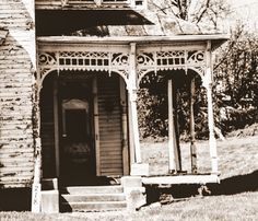 black and white photograph of an old house with porch, stairs and front door in the foreground