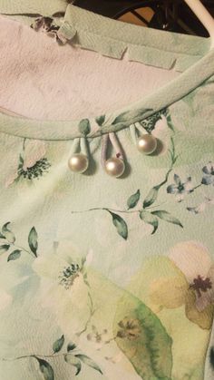 two pearls are attached to the back of a green floral dress with white flowers on it