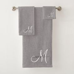 two gray towels with monogrammed names hanging on a towel rack in front of a white wall