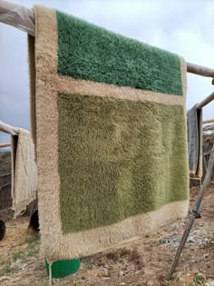 a green and beige blanket hanging on a clothes line in the dirt near a fence