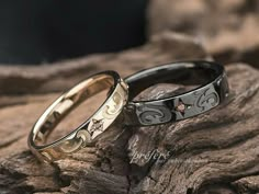 two wedding rings sitting on top of a wooden log next to another ring with hearts