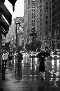 black and white photograph of people walking in the rain with umbrellas on a city street