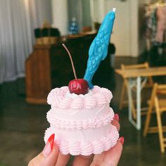 a hand holding a small cupcake with a cherry on top and a blue candle sticking out of it