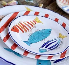 colorful plates with fish painted on them stacked on top of each other in front of a wooden table