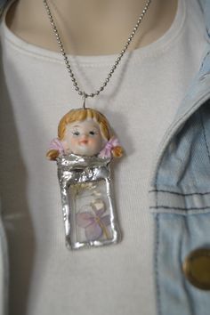 a woman wearing a necklace with a little doll in it's pocket on a chain