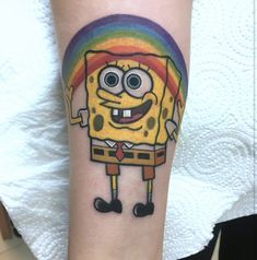 a spongebob tattoo on the arm with a rainbow in the background and a cartoon character