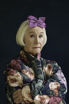 an older woman with her arms crossed wearing a flowery jacket and purple bow tie