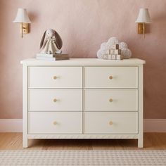 a white dresser sitting in front of a pink wall with two lamps on top of it