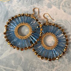 a pair of blue and gold beaded earrings on top of a patterned table cloth