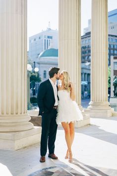 a man and woman standing next to each other in front of pillars