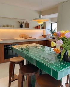 a green tiled table with stools and flowers in a vase on the counter top