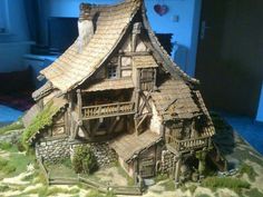 a house made out of wood and stone with grass growing on the roof is shown in front of a blue wall