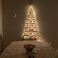 a lighted christmas tree sitting on top of a bed next to a bowl filled with ornaments