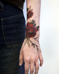 a woman's hand with a red flower tattoo on her left arm and wrist