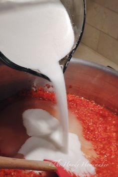 a ladle pouring milk into a pot filled with red sauce