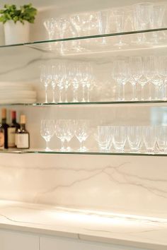 wine glasses are lined up on glass shelves in a kitchen with white marble countertops