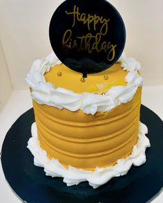 a yellow and white birthday cake with a black happy birthday sign on it's top