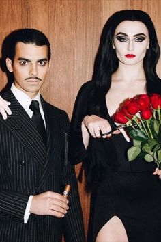 a man and woman dressed in black standing next to each other with roses on their lap