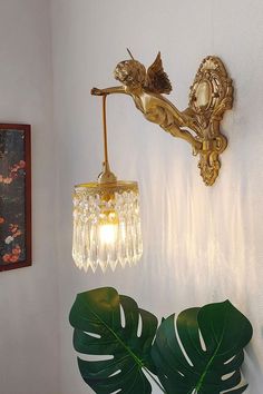 a wall mounted light next to a large green leafy plant on a white wall