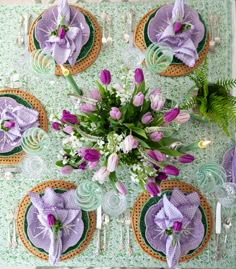 the table is set with purple flowers and green placemats, silverware, and napkins