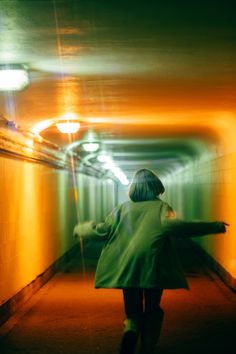 a woman in a green coat is walking down a long tunnel with her arms outstretched