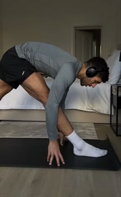 a man is stretching on a mat in the middle of a room with a bed behind him