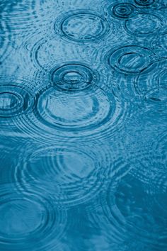 rain drops falling on the surface of blue water with ripples and circles around them