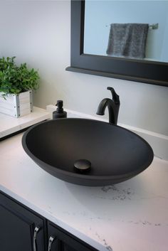 a black bowl sink sitting on top of a counter next to a mirror and potted plant