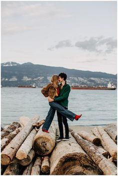 a man and woman are hugging on logs by the water