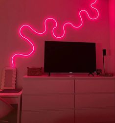 a television sitting on top of a white dresser under a neon pink light in a room