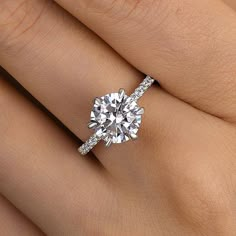 a woman's hand with a diamond engagement ring on her left hand and the center stone is surrounded by pave diamonds