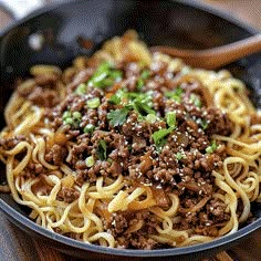 a close up of a plate of food with noodles and ground beef in it on a wooden table