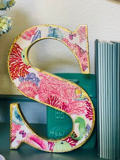 the letter s is decorated with colorful flowers and books on a shelf next to a vase