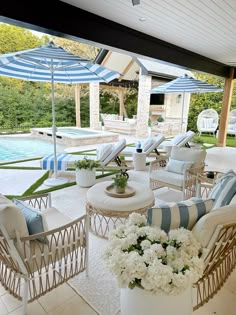 an outdoor living area with chairs, tables and umbrellas next to a swimming pool