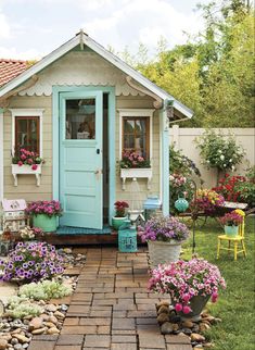 a small garden shed with potted plants and flowers in the front yard, next to a patio