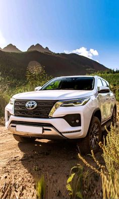 the front end of a white suv driving down a dirt road near mountains and trees