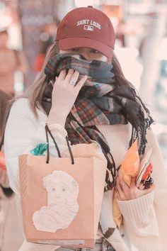 a woman with a hat and scarf holding a shopping bag while talking on the phone