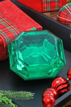 a green jewel surrounded by red and green christmas presents on a black tray with ornaments