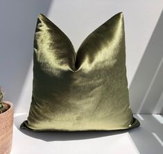 a green pillow sitting on top of a white table next to a potted plant