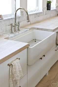 a white kitchen sink sitting under a window next to a counter top with a towel hanging on it