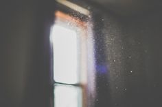 an open window in a dark room with sunlight coming through the window panes and snow falling on the floor